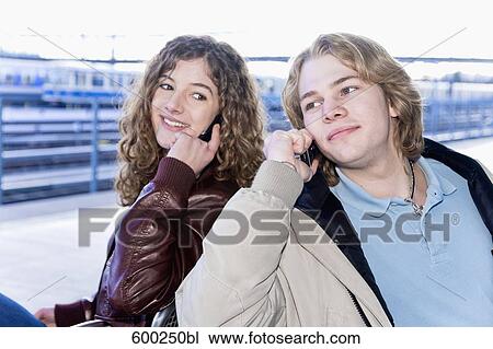 teenage couple sitting on bench at station talking on mobile phones View Large Photo Image Stock Image - teenage couple sitting on bench at station talking on mobile phones. Fotosearch