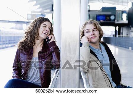 teenage couple sitting on bench at station talking on mobile phones View Large Photo Image Stock Image - teenage couple sitting on bench at station talking on mobile phones. Fotosearch