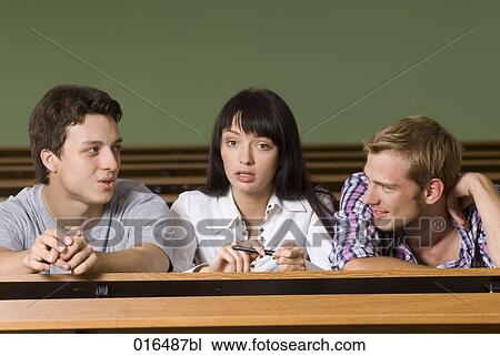 Stock Image - three young students sitting in lecture hall having a conversation. Fotosearch