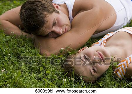 Stock Image - young couple lying on lawn in park man looking at woman. Fotosearch
