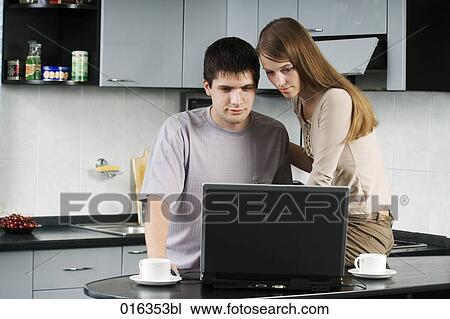 young couple sitting together in the kitchen looking at laptop computer View Large Photo Image Stock Image - young couple sitting together in the kitchen looking at laptop computer. Fotosearch