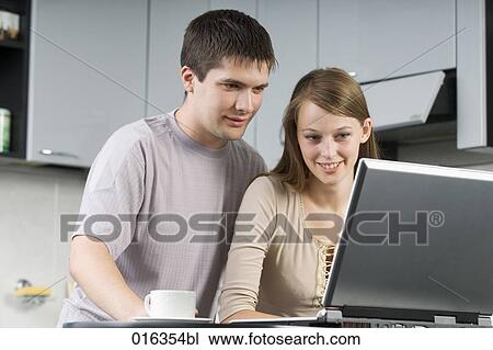 young couple sitting together in the kitchen looking at laptop computer View Large Photo Image Stock Image - young couple sitting together in the kitchen looking at laptop computer. Fotosearch