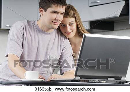 young couple sitting together in the kitchen looking at laptop computer View Large Photo Image Stock Image - young couple sitting together in the kitchen looking at laptop computer. Fotosearch