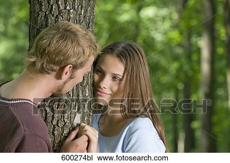 young couple standing at tree tenderly looking at each other View Large Photo Image Stock Image - young couple standing at tree tenderly looking at each other. Fotosearch