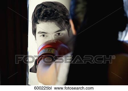 Stock Image - young female boxer hitting punching bag with photo of former boyfriend. Fotosearch