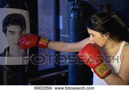 Stock Image - young female boxer hitting punching bag with photo of former boyfriend. Fotosearch
