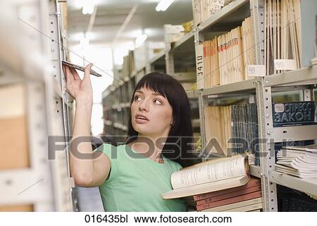 Stock Image - young female student looking for books in school library. Fotosearch