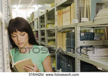 Stock Image - young female student reading textbook in school library. Fotosearch
