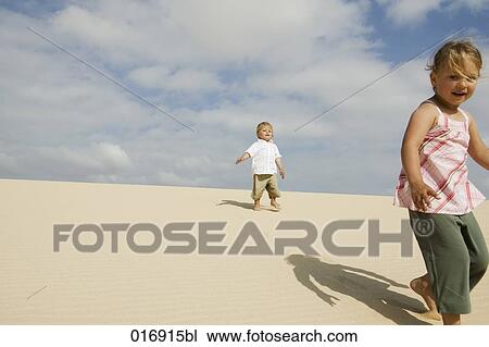 Stock Image - young girl and little brother walking on sandy beach. Fotosearch