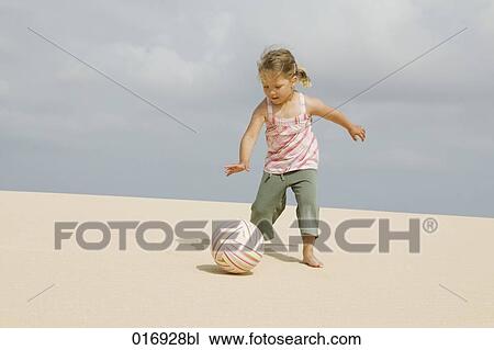 Stock Image - young girl kicking ball on sandy beach. Fotosearch