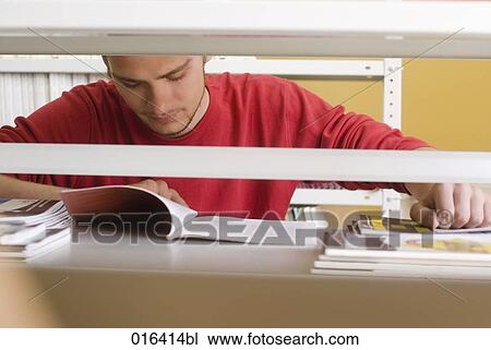 Stock Image - young male student reading textbook in school library. Fotosearch