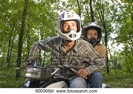 Stock Image - young man and girlfriend driving on quad through forest. Fotosearch