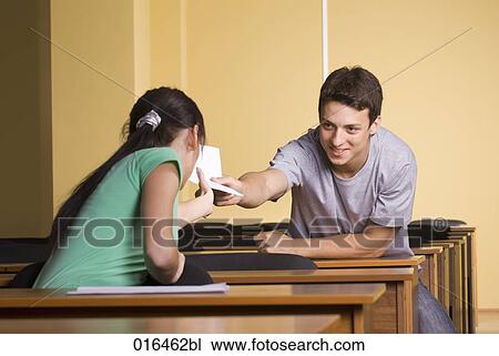 Stock Image - young man giving document to female student during school seminar. Fotosearch