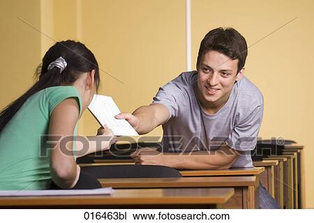 Stock Image - young man giving document to female student during school seminar. Fotosearch