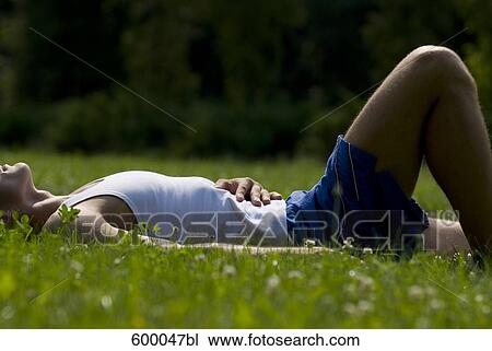 Stock Image - young man in sportswear relaxing on lawn in park. Fotosearch