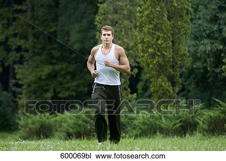 Stock Image - young man jogging through park and listening to music. Fotosearch