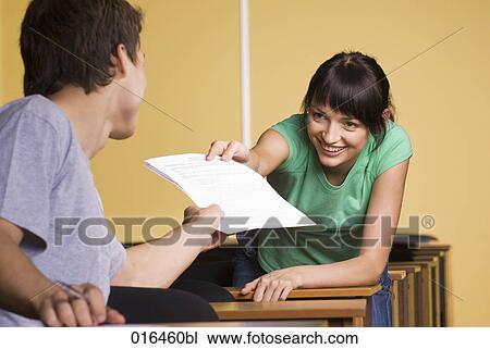 Stock Image - young woman giving document to male student during school seminar . Fotosearch