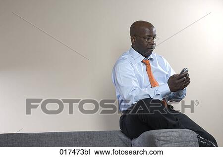black businessman sitting on armrest of sofa checking mobile phone for text messages View Large Photo Image Stock Image - black businessman sitting on armrest of sofa checking mobile phone for text messages. Fotosearch