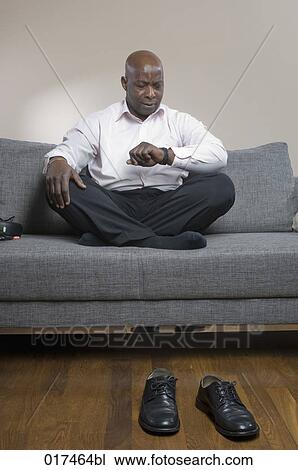 Stock Image - black businessman sitting on sofa looking at his watch. Fotosearch