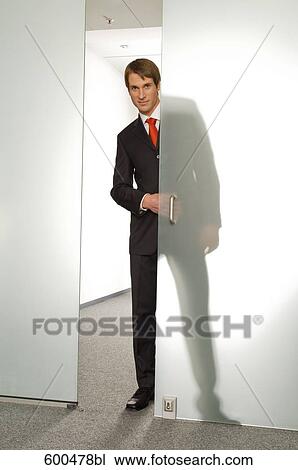 Stock Image - businessman peeking behind half open glass door. Fotosearch
