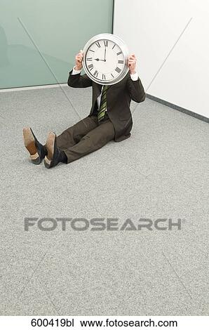 Stock Image - businessman sitting in corner hiding behind clock. Fotosearch