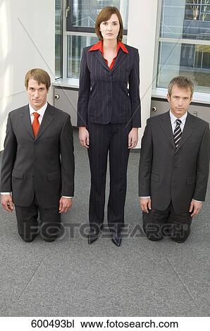 Stock Image - businesswoman standing between kneeling male colleagues. Fotosearch