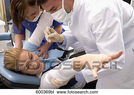 Stock Image - dentist and assistant trying to examine fearful patient. Fotosearch