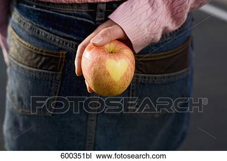 Stock Image - detail of young woman holding apple with shape of heart on it. Fotosearch