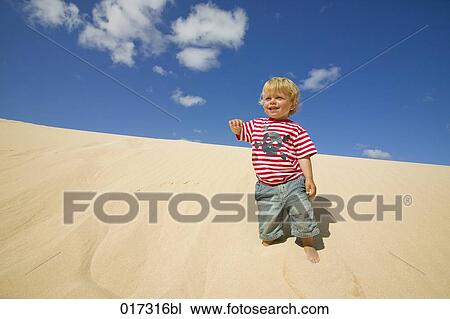 Stock Image - full body portrait of little boy on sand dune. Fotosearch