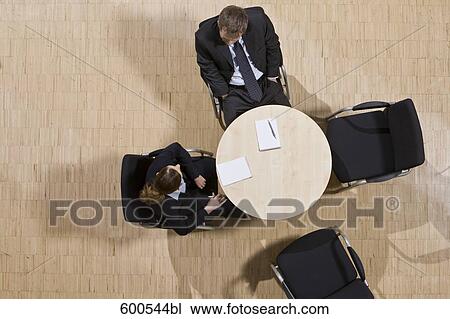 Stock Image - high angle view of group of business people sitting around conference table. Fotosearch