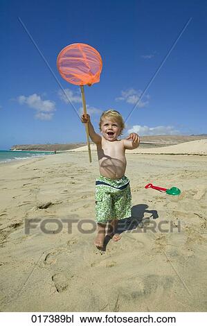 Stock Image - little boy walking along beach holding spoon net. Fotosearch