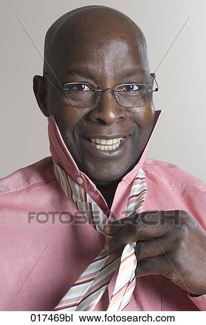 Stock Image - portrait of black businessman putting on tie. Fotosearch