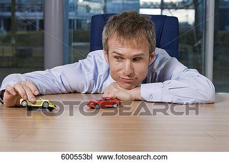 Stock Image - portrait of businessman playing with toy cars. Fotosearch