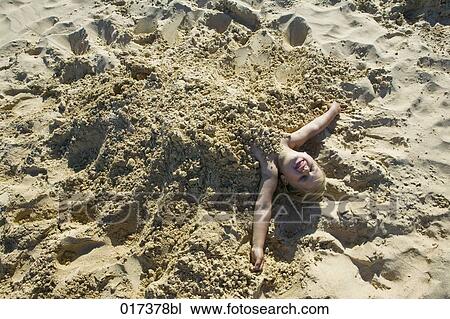 Stock Image - portrait of young girl buried in sand on beach. Fotosearch