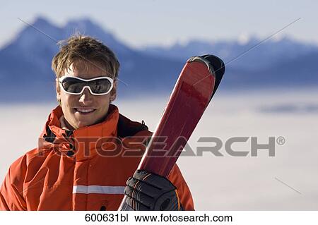 Stock Image - portrait of young in the mountains holding skis. Fotosearch