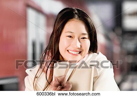 Stock Image - portrait of young japanese woman at train station holding present. Fotosearch