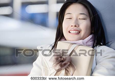Stock Image - portrait of young japanese woman waiting with present at train station. Fotosearch