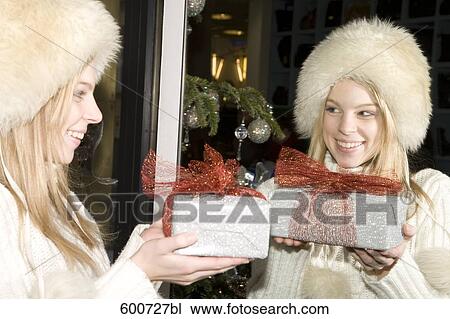 Stock Image - portrait of young with christmas present looking at herself in the mirror. Fotosearch