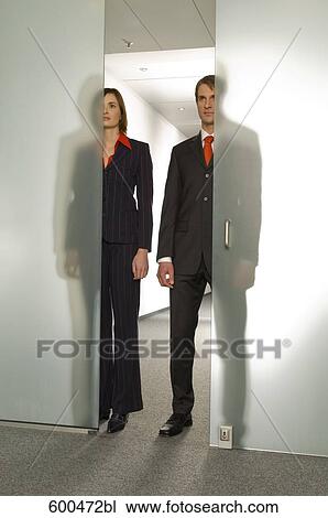 Stock Image - two business people standing side by side behind half open glass door. Fotosearch