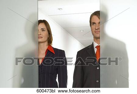 Stock Image - two business people standing side by side behind half open glass door. Fotosearch
