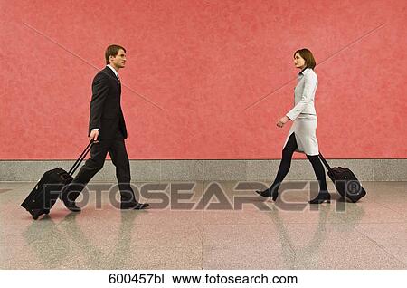 Stock Image - two business travellers in corridor pulling carry-on suitcases. Fotosearch