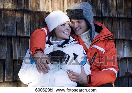 Stock Image - young couple in winter clothes embracing woman holding mug. Fotosearch