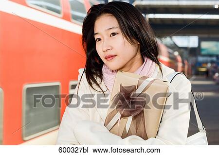 Stock Image - young japanese woman waiting with present at train station. Fotosearch