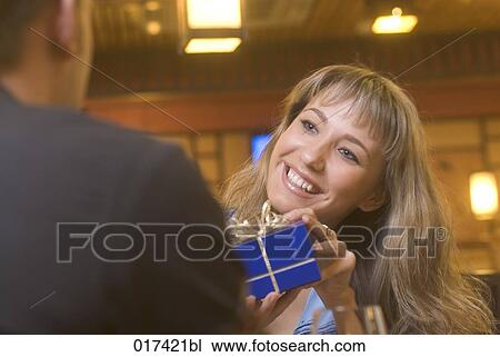 Stock Image - young woman getting present from boyfriend in restaurant. Fotosearch