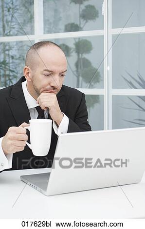 businessman with cup looking at laptop computer View Large Photo Image Stock Image - businessman with cup looking at laptop computer. Fotosearch