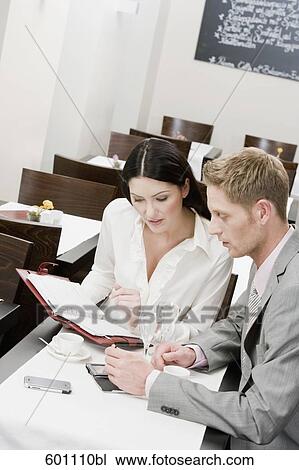 Stock Image - businesswoman and male colleague at restaurant reading document. Fotosearch