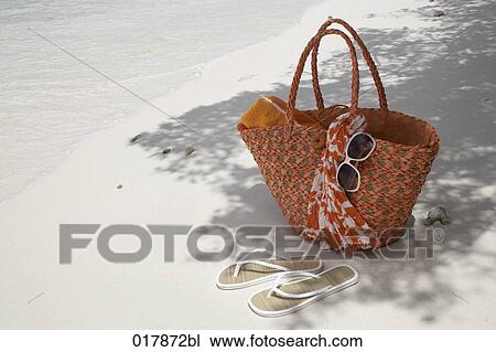Stock Image - flip flops bag and sunglasses on sandy beach. Fotosearch