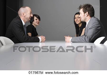 Stock Image - four business people sitting around conference table. Fotosearch