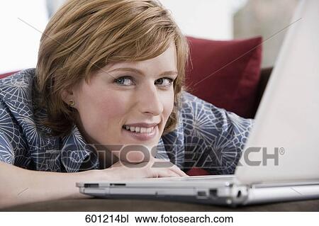 Stock Image - headshot of young woman at home working with laptop computer. Fotosearch