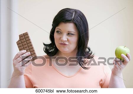 Stock Image - overweight woman choosing between chocolate and apple. Fotosearch